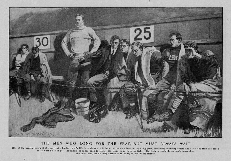 COLLEGE FOOTBALL SUBSTITUTES SIT ON SIDELINE WAITING TO PLAY UNIVERSITY COACH